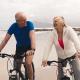 An active senior couple riding bicycles on a beach.