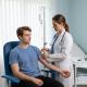A doctor in a white coat and stethoscope is preparing to administer an IV to a young male patient sitting in a chair.